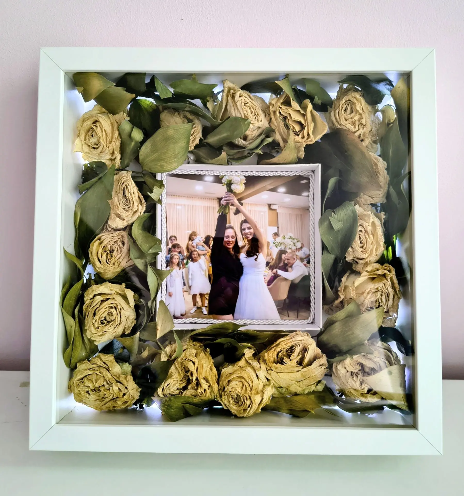 съхранение на сватбен букет в рамка завинаги. снимка на булката и жената, хванала букета. Държат букета високо над главите си. около снимката са аранжирани цветята от самия букет. Рози. роза