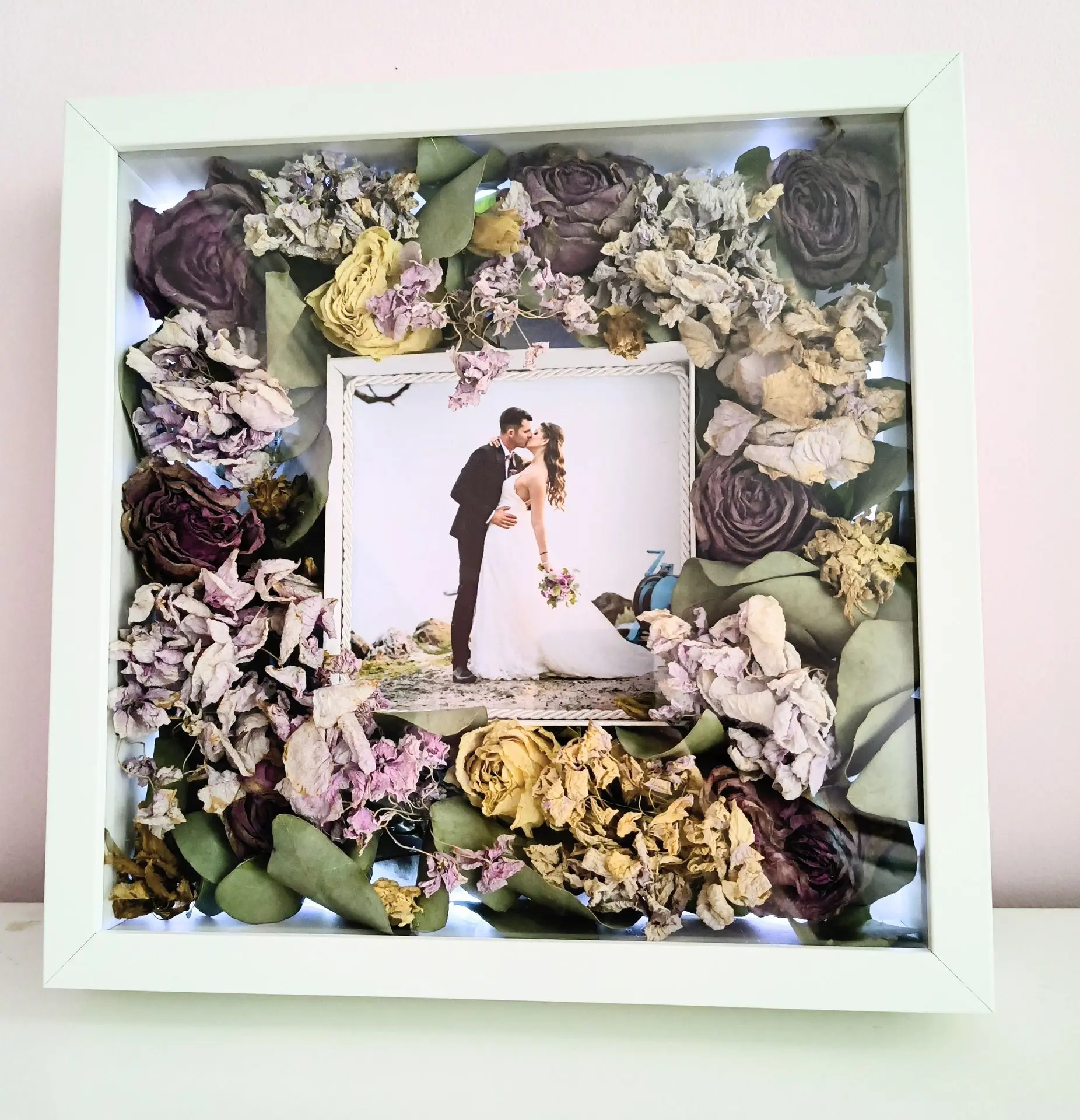 Сватбен букет в рамка. Снимка на младоженците, които се целуват, а около тях е разпределен букетът на булката